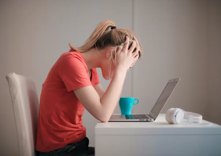 Une femme ayant le burn-out face à son ordinateur. Elle pose les mains sur sa tête.