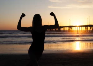 Une femme musclée à contre jour, soleil couchant sur la plage pour illustrer l'article de blog : Les leçons que les femmes peuvent enseigner aux hommes.