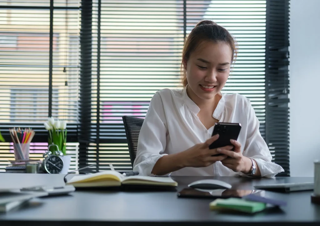 Un femme entrepreneure dans son bureau sur son téléphone en train de démarcher des clients à distance.
